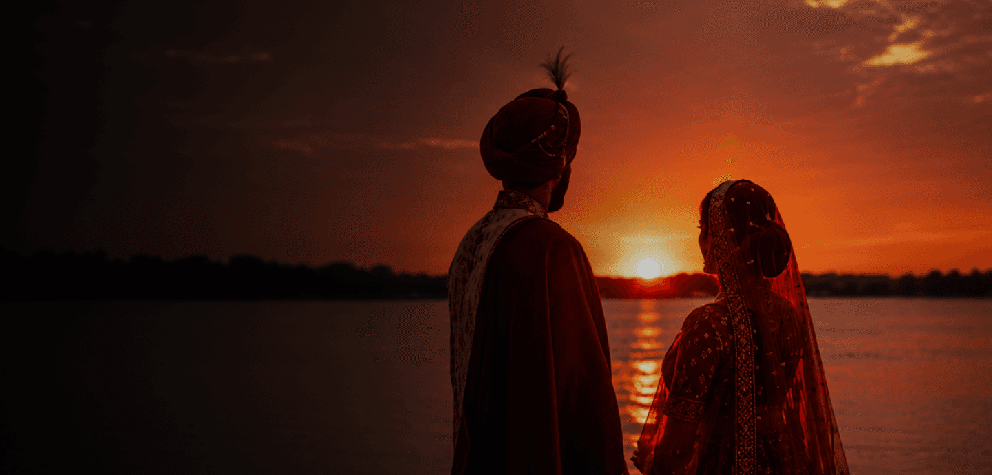 Couple in traditional wedding attire watching the sunset over water